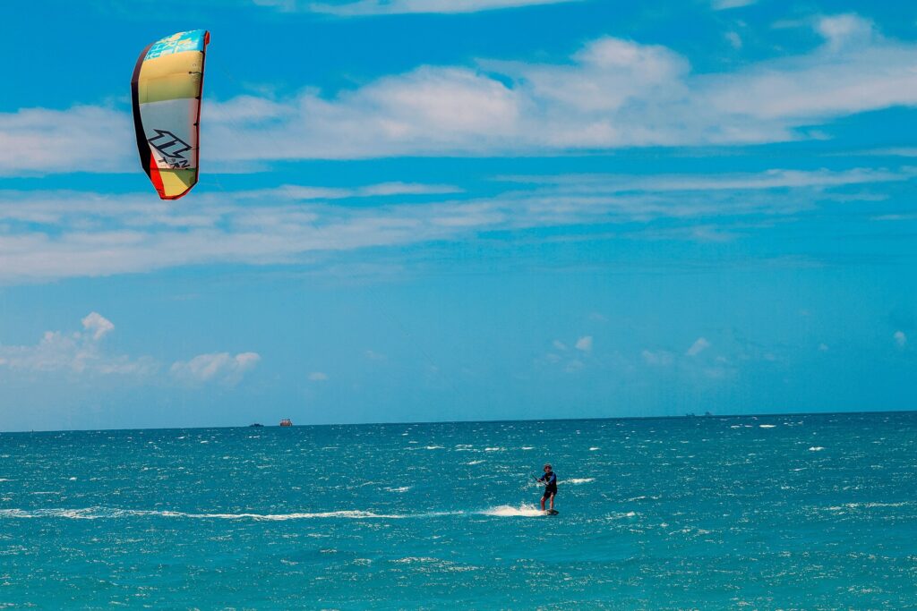 A kitesurfer catching air above the waves on Paje Beach, Zanzibar."
"Beginner kitesurfing lesson at Paje Beach, with an instructor guiding a student in shallow waters."
"A panoramic view of Paje Beach, Zanzibar, with kitesurfers in the distance and turquoise waters meeting the sandy shore."
"Palm trees lining the white sandy shores of Zanzibar Island under a clear, sunny sky."
"The entrance of a kitesurf school in Paje, Zanzibar, featuring surfboards and kites ready for lessons."
"A group of kitesurfing students preparing their kites on the beach at a kitesurf school in Zanzibar."
"Traditional dhow sailing near the coast of Zanzibar Island at sunset, reflecting the island’s rich cultural heritage."
"Stone Town’s vibrant market, showcasing the cultural side of Zanzibar, with colorful stalls and local products."